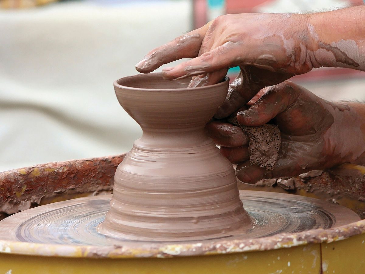 Hands shaping a clay pot on a spinning potter’s wheel