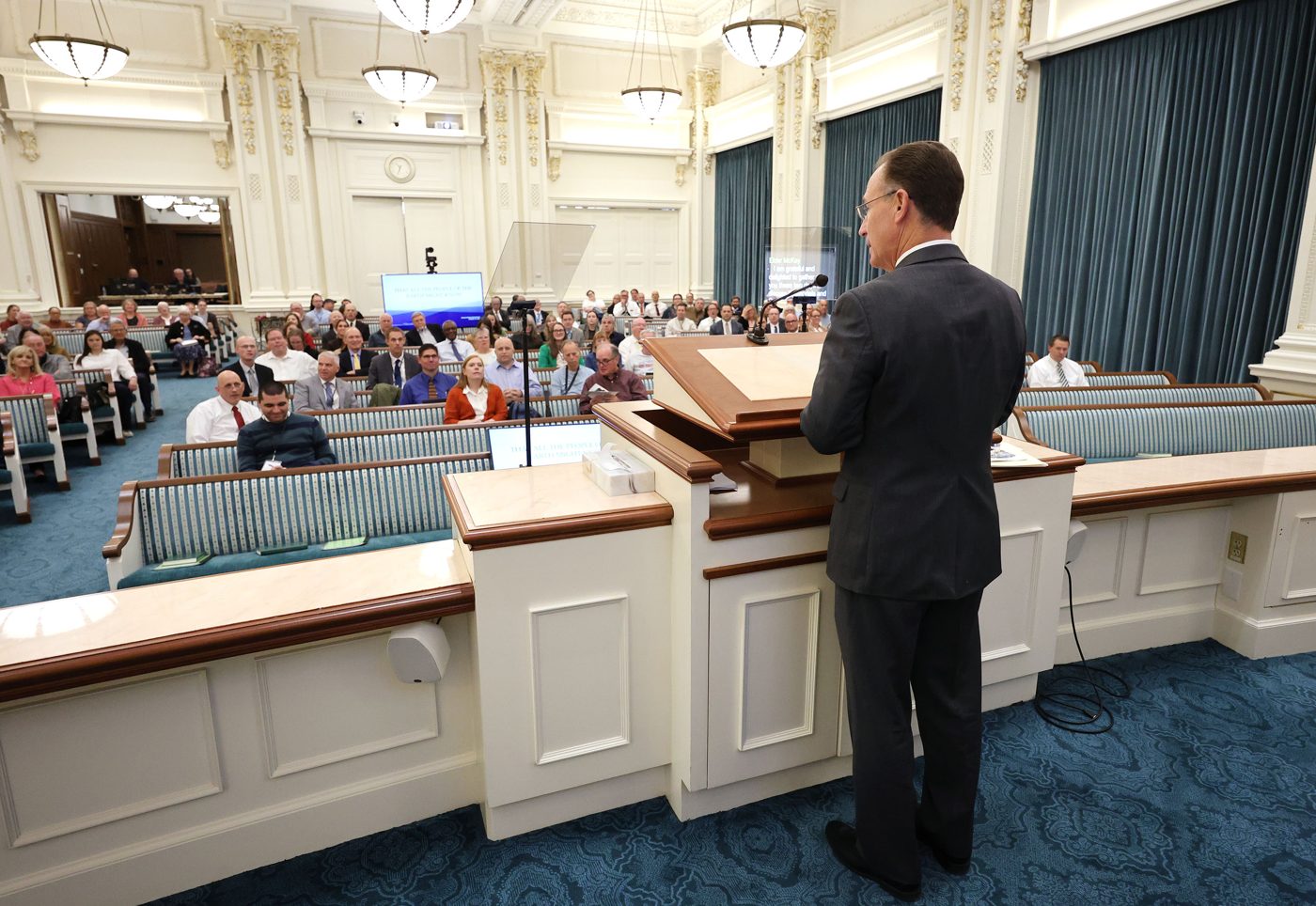 Elder Kyle S. McKay speaking at a pulpit to attendees in the Joseph Smith Memorial Building chapel