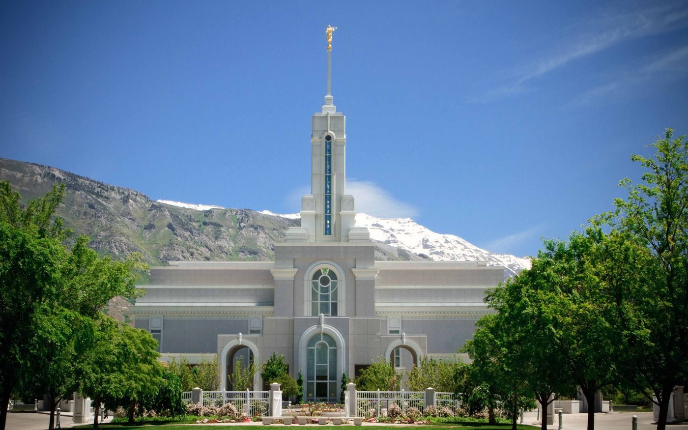 The white Mount Timpanogos Utah Temple with its single spire below snowy mountains