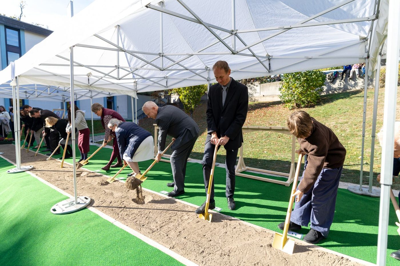 Leaders turning shovels of soil under a white tent at the Vienna Austria Temple groundbreaking